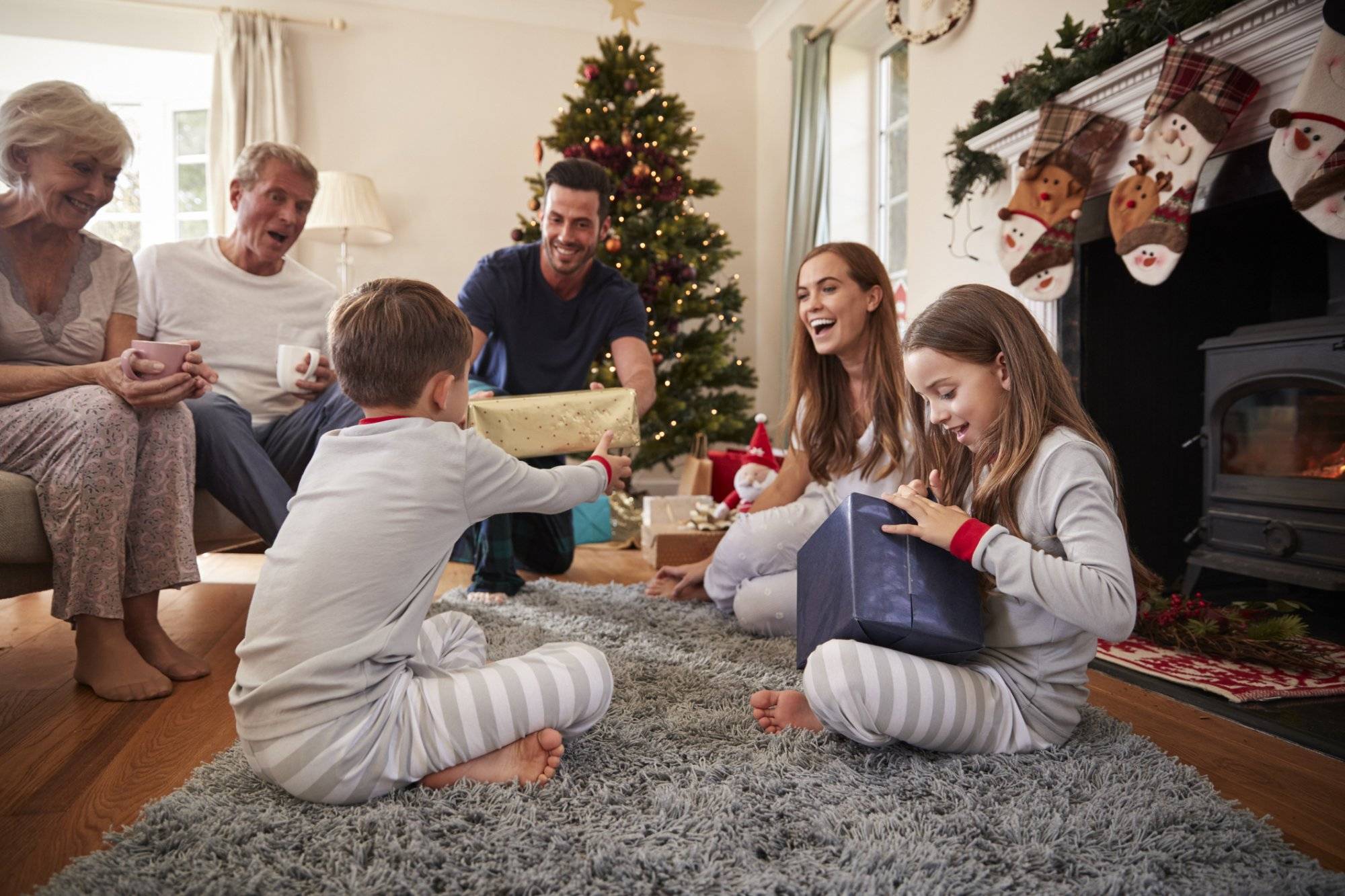 Three Generation Family Wearing Pajamas In Lounge At Home Opening Gifts On Christmas Day Three Generation Family Wearing Pajamas In Lounge At Home Opening Gifts On Christmas Day