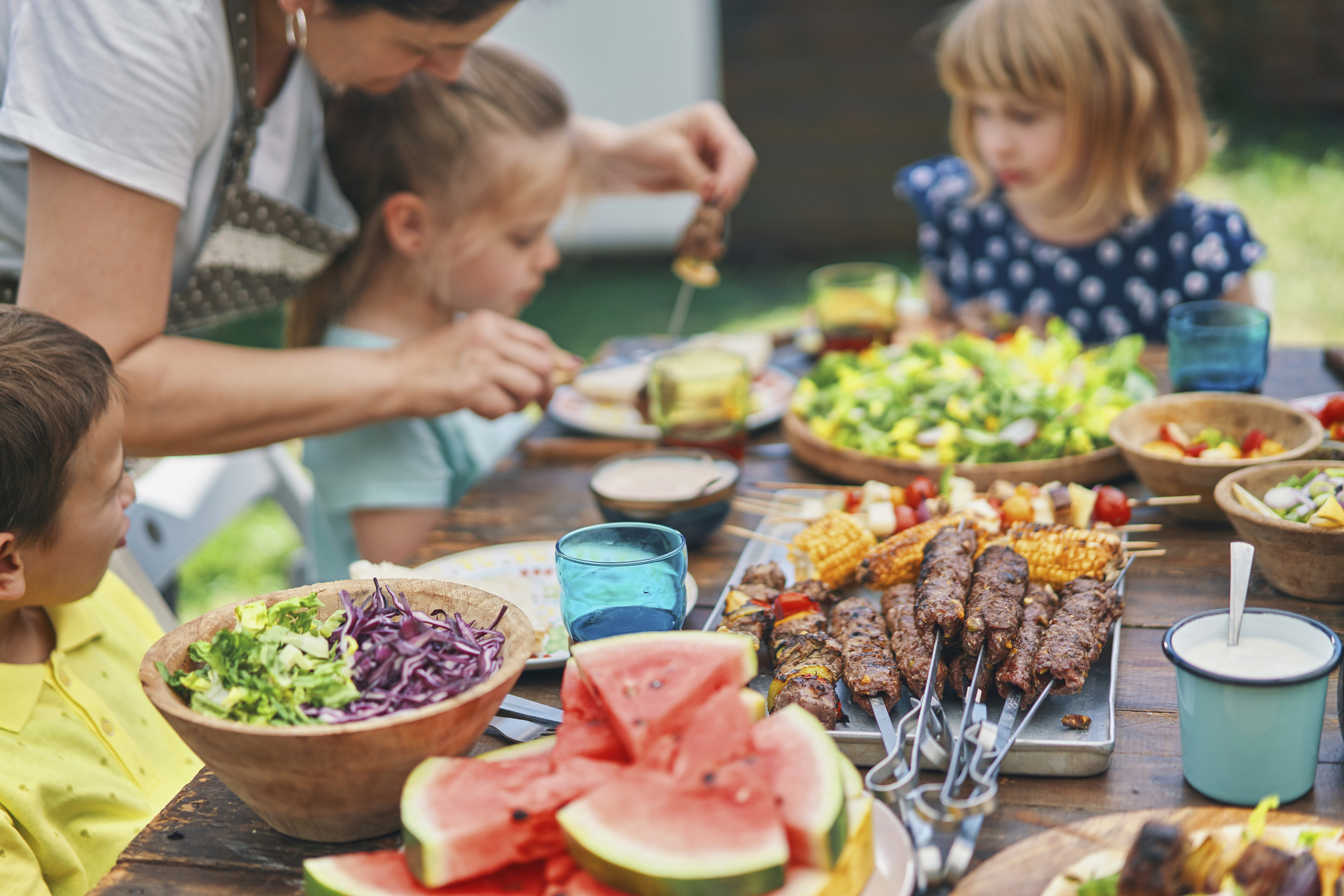 Young Family Eating Lamb, Beef and Vegetable Kebab with Green Salad Outside