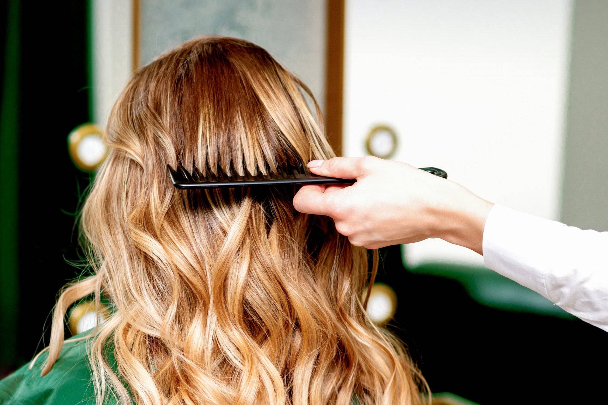 Hairdresser combing wavy hair of woman