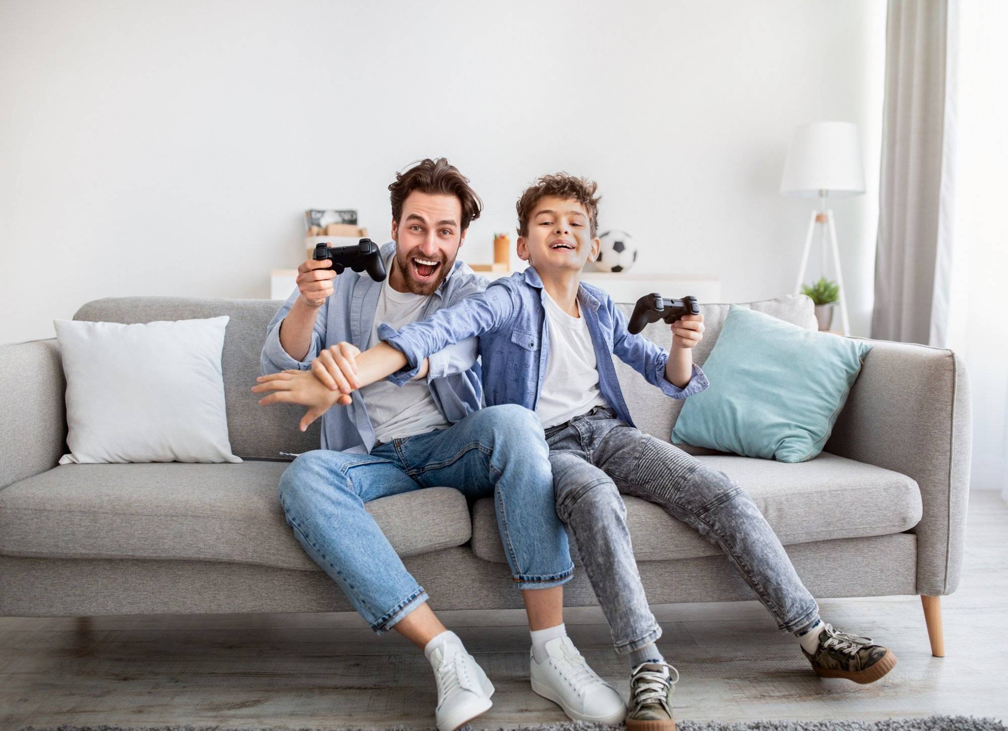 Joyful dad and son with joysticks playing video games at home, boy distracting father with hand Joyful dad and son with joysticks playing video games at home, boy distracting father with hand