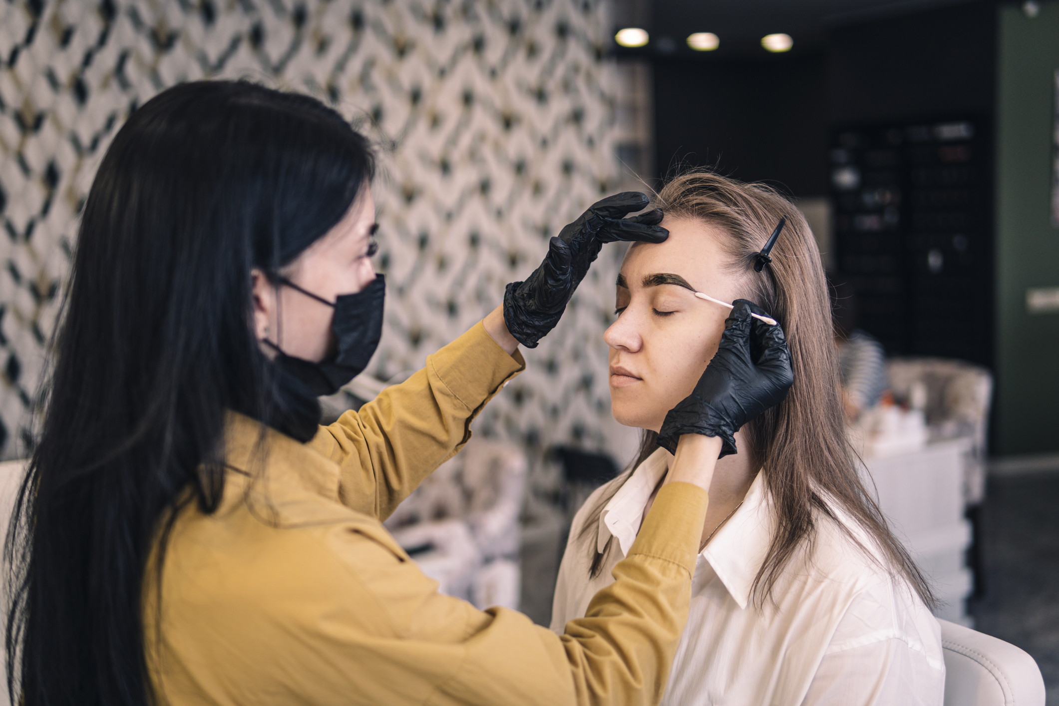 A master cosmetologist paints the eyebrows of a client in the salon close-up. eyebrow dyeing procedure, girl wipes paint from her eyebrows.
