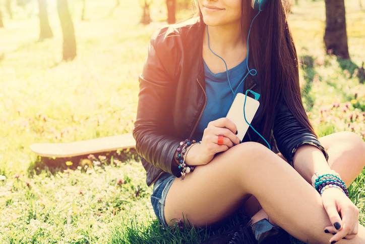 Teenage girl with smartphone sitting in the grass