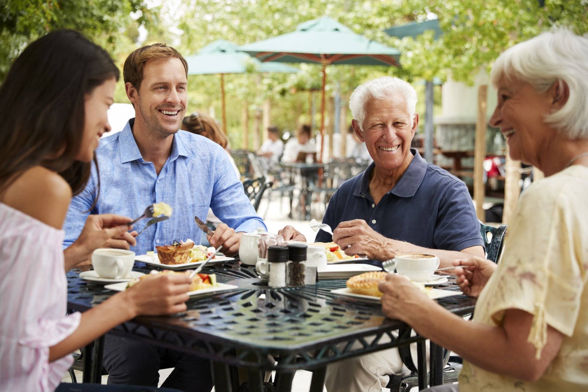 Senior Parents With Adult Children Enjoying Meal At Outdoor Cafe